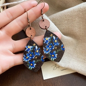 Handheld shot of teardrop bohemian wood earrings featuring blue daisy floral patterns