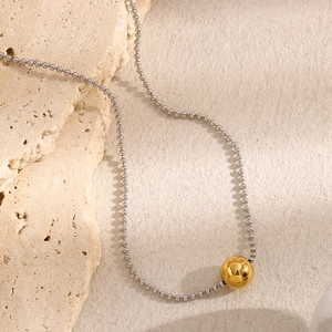 Close-up of a silver bead chain necklace with a polished 18K gold-plated ball pendant