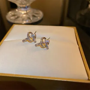 Knot earrings in gold finish with micro-pave cubic zirconia on a beige cushion