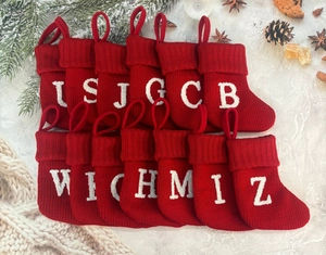 Flat lay of mini red knitted Christmas stockings with white alphabet embroidery on marble