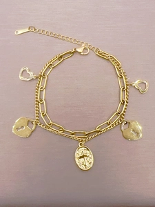 Detail eines goldenen zweischichtigen Armbands mit Herz-, Schloss- und Kreuzanhänger