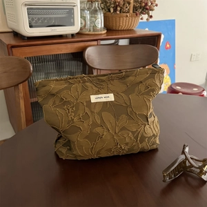 Detailed view of caramel brown jacquard makeup bag with floral embroidery and fabric label
