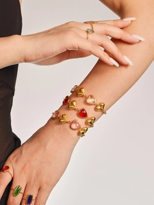 Primer plano de pulseras de corazón doradas con piedras de cristal rojas y rosas en la muñeca