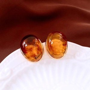 Detailed macro view of caramel amber resin earrings with gold trim on ceramic plate