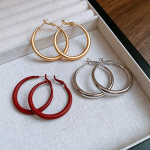 Detailed view of metal hoop earrings in gold brushed, silver polished, and red matte finishes
