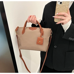 Detail of khaki nylon tote bag featuring brown leather handles and brand logo tag