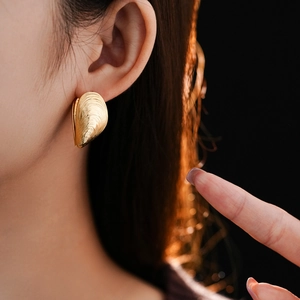 Close-up of a gold shell-shaped earring with threaded texture on a model's ear