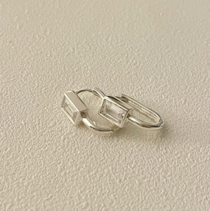 Detail of silver huggie earrings with rectangular cubic zirconia on a textured surface