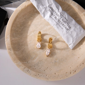 Close-up of golden teardrop zircon earrings on a beige stone tray with a natural light setup