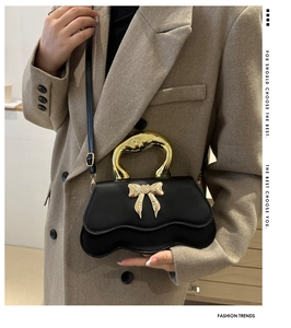 Detail of black handbag with gold metal handle and bow clasp on beige coat