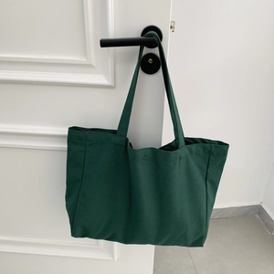 Close-up of a large dark green canvas tote bag hanging on a minimalist white door handle
