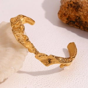 Detail view of gold wave bangle with organic hammered texture and water droplets