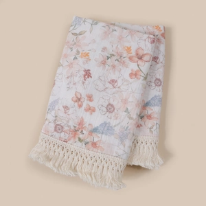 Detail of floral cotton baby blanket with elegant fringe trim and soft muslin gauze texture.