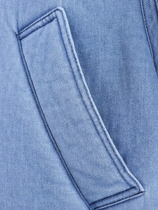 Close-up of side pocket on light blue washed denim jacket with double-needle stitching