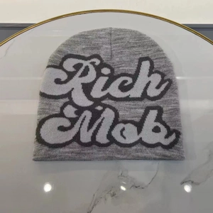 Detail of grey knitted beanie featuring 3D Rich Mob letter embroidery on marble surface