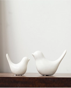 Close-up of a pair of large and small white ceramic bird figurines on a wooden surface