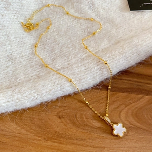 Detail of gold beaded chain necklace with a white four-leaf clover pendant on fabric