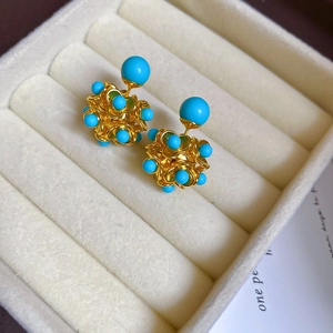 Macro view of gold hollow sphere earrings with blue turquoise beads on white velvet