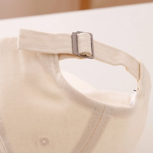 Detail of light beige twill cotton baseball cap with adjustable dark grey metal buckle