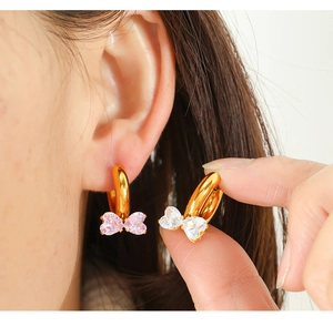 Detailed close-up of gold bow earrings featuring pink and clear cubic zirconia stones