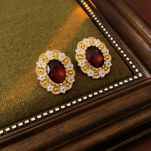 Close-up of vintage gold earrings with deep red oval gems and white enamel floral accents