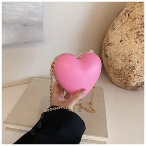 Pink heart-shaped hard shell clutch with gold chain strap held to show mini size