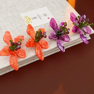 Detail of vintage flower earrings in orange and purple acrylic with bead centers on a book
