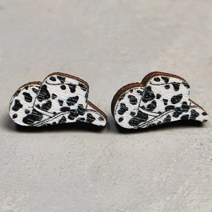 Detailed macro view of wooden cowboy hat stud earrings with black and white cow print texture