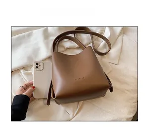 Brown bucket bag size comparison with a white smartphone on a minimalist background