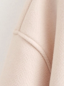 Macro shot of beige wool jacket fabric showing soft texture and high-quality seam details
