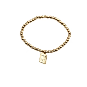 Gros plan d'un bracelet élastique à billes dorées avec pendentif carré gravé de la lettre K