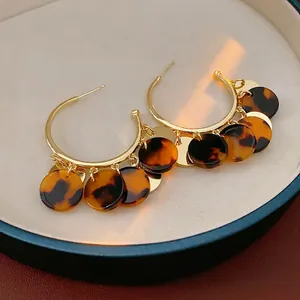 Golden C-shaped earrings with leopard print tortoiseshell circles on white jewelry tray