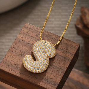 Macro shot of 18K gold plated letter S pendant with zircon stones on a wooden block