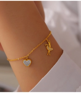 Close-up of gold-plated titanium bracelet featuring a crystal heart and ballerina pendant