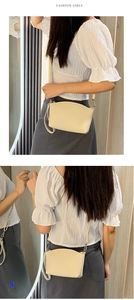 Detail showing a minimalist cream crossbody bag worn by a model against a wooden wall