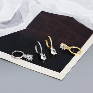 Détail de créoles en argent et or avec pendentifs en zircon brillant sur fond de bois