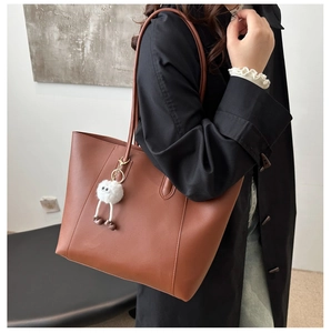 Detail view of large brown faux leather tote bag with a cute white plush pendant