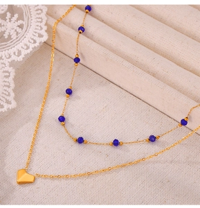 Detail view of double-layered gold necklace with heart pendant and blue beads