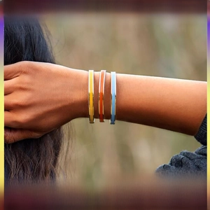 Three stacked enamel bangle bracelets in yellow, orange, and blue on a woman's wrist