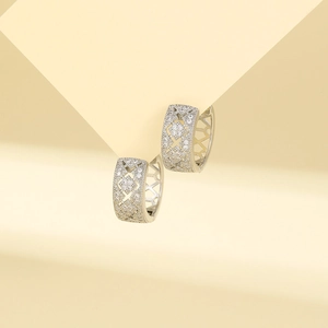 Detailed close-up of geometric silver earrings with pavé zircon stones on yellow background