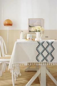 Detail of beige linen tablecloth with blue geometric embroidery and white tassel edge