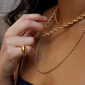 Detail of layered gold twist chain necklace and smooth band ring worn by model