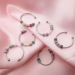 Stack of silver fidget rings with colorful enamel beads on a soft pink silk background