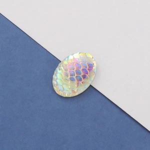 Macro shot of oval white resin cabochon with colorful AB fishtail scale pattern