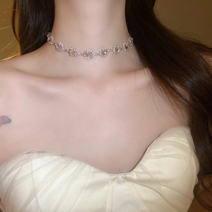 Close-up of a silver choker necklace featuring pink heart stones and diamond halo details