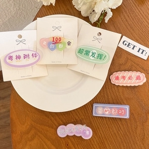Detail of colorful matte hair clips with lucky exam phrases on white ceramic plate