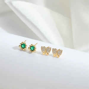Elegant gold butterfly stud earrings with green gemstone set on white fabric