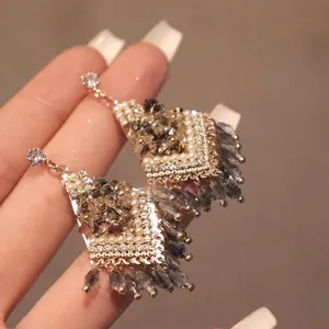 Vintage gold drop earrings with pearls and crystals shown in a hand-held display