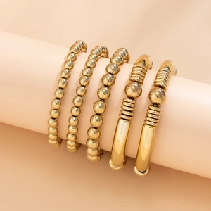 Detailed stack of gold beaded bracelets and metal cuffs on a soft pink display stand