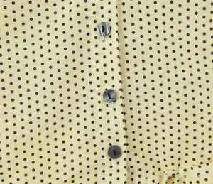 Detailed close-up of yellow polka dot fabric with iridescent grey button closure